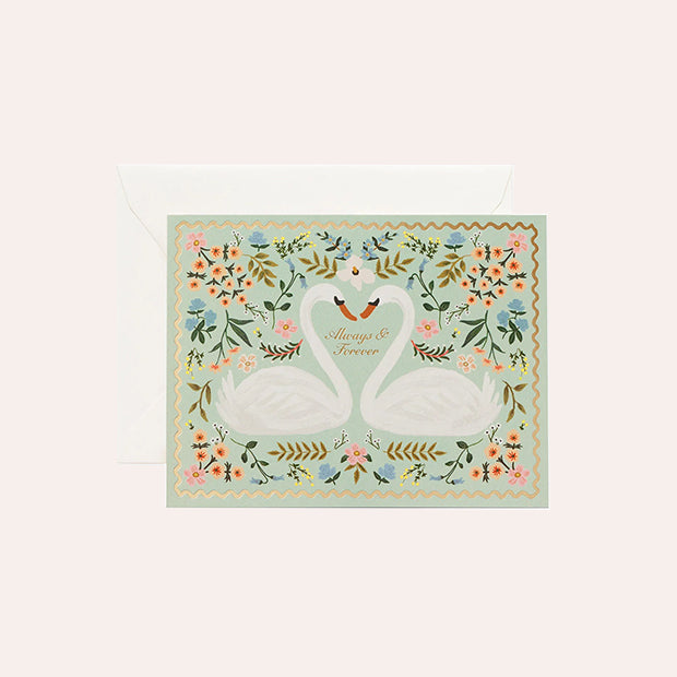 Rifle Paper Co Always &amp; Forever wedding greeting card featuring two white swans forming a heart, surrounded by colourful flowers on a pale mint green background, with a white envelope.
